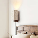 Sconce lit above a slatted wood headboard and a bed with pale pillows