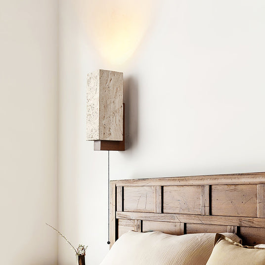 Sconce lit above a slatted wood headboard and a bed with pale pillows
