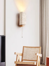 Sconce lit beside a curtain above a cane backed chair in a quiet corner