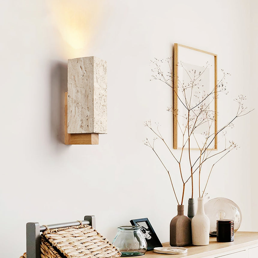 Sconce lit above a console with a vase of branches and a leaning frame