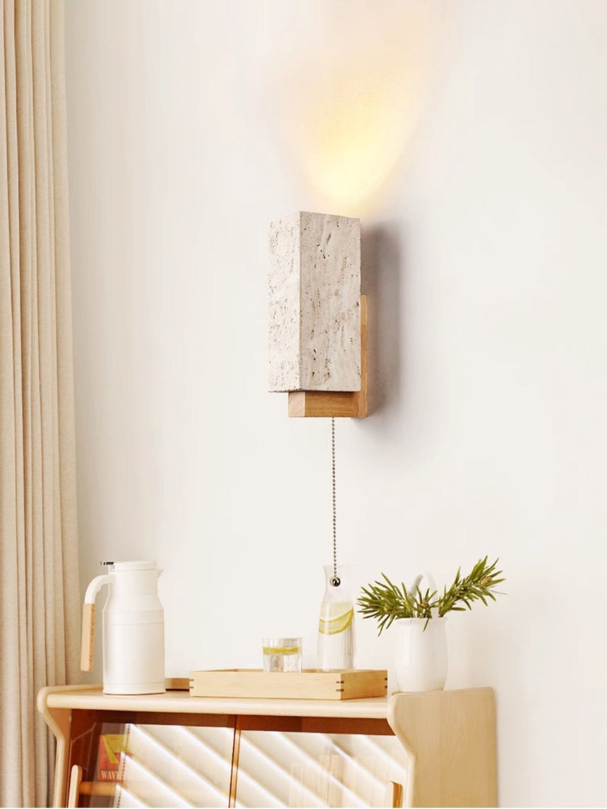 Sconce lit above a side table holding a jug, two cups and a small plant