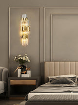 The sconce lit above a nightstand with flowers beside an upholstered bed
