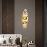 The sconce lit on a dark herringbone wall above a bed and a nightstand