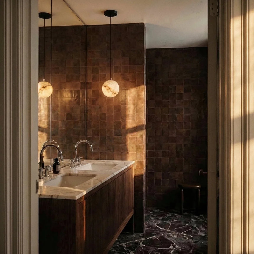 A lit stone sphere beside a mirror above a basin in a dark tiled bathroom