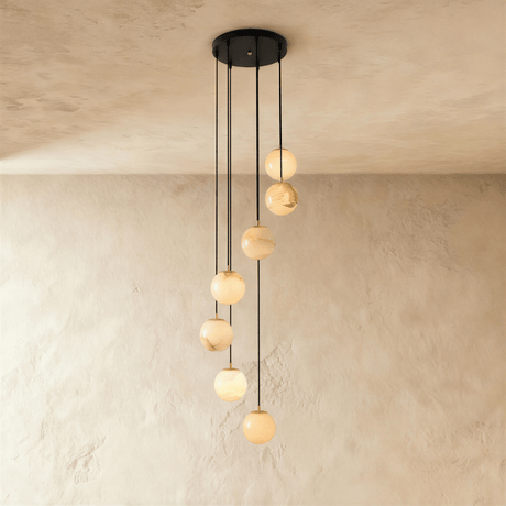 Seven lit alabaster spheres spread down a plaster wall on black cords