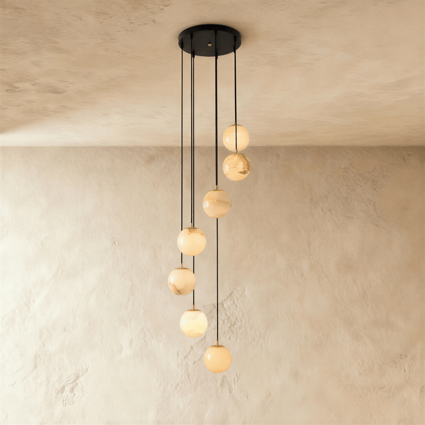 Seven lit alabaster spheres spread down a plaster wall on black cords