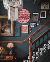 Hung in a stairwell above a gallery wall of framed pictures and a banister