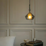 The faceted shade lit against a paneled wall above a console and vase