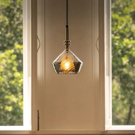 The faceted shade lit beside a window with green leaves behind it