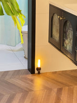 Lit low beside a fireplace on a herringbone floor, the beam washing the boards