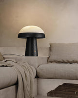 Stone table lamp lit beside a pale sofa and a folded throw