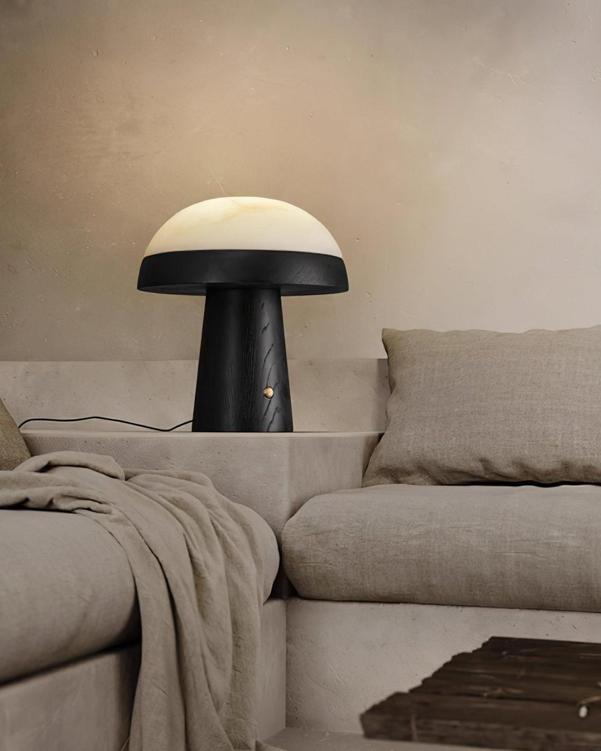 Stone table lamp lit beside a pale sofa and a folded throw