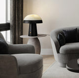 Stone table lamp lit on a side table between two gray armchairs
