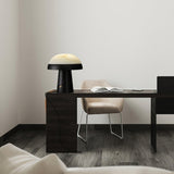 Stone table lamp with a black base lit on a dark desk