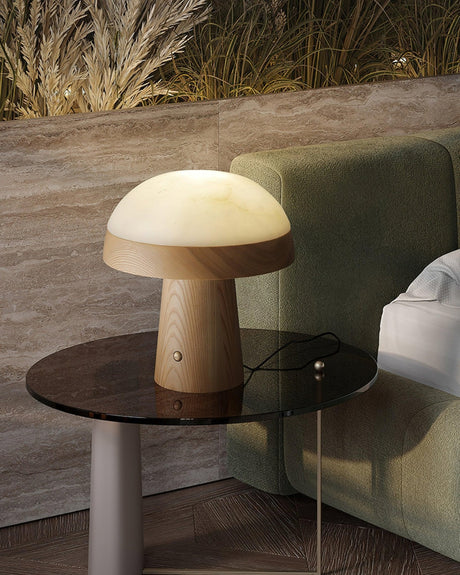 Stone table lamp lit on a glass side table beside a green headboard