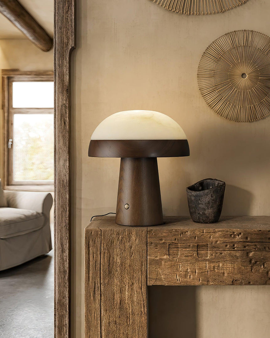 Stone table lamp lit on a rustic wood console in a pale room