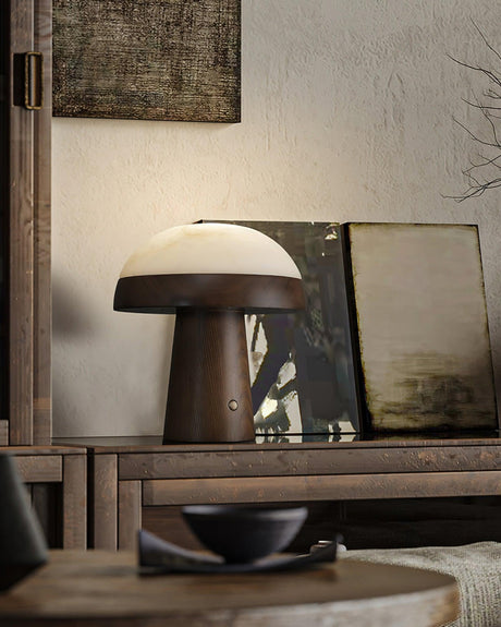 Stone table lamp lit on a console beside leaning framed art