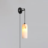 The blackened brass version lit, hanging on a plain gray wall