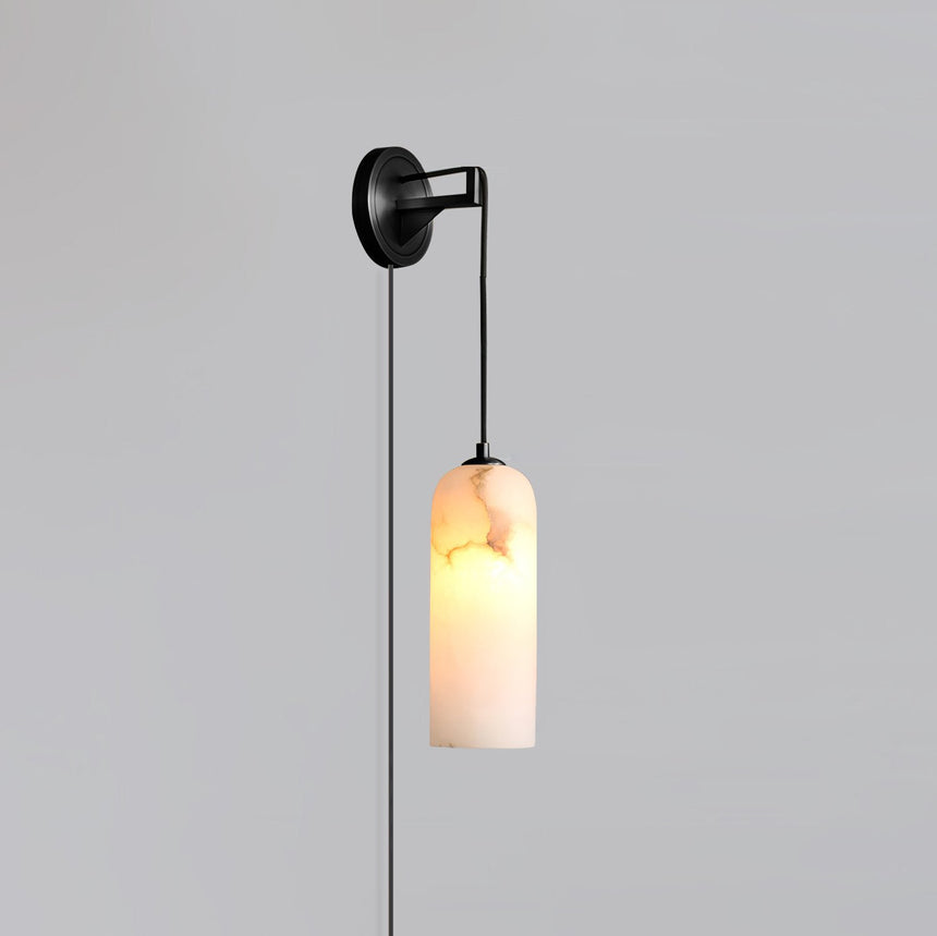 The blackened brass version lit, hanging on a plain gray wall