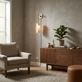 The lit lamp above a walnut cabinet beside an armchair and a plant