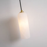 The stone cylinder lit warm, hanging from its cord on a pale wall