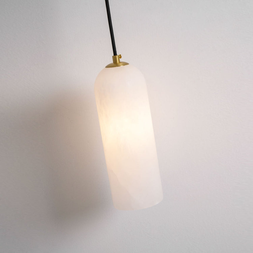 The stone cylinder lit warm, hanging from its cord on a pale wall