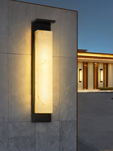 The light on a stone clad facade with a lit building further behind