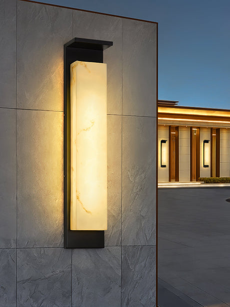 The light on a stone clad facade with a lit building further behind