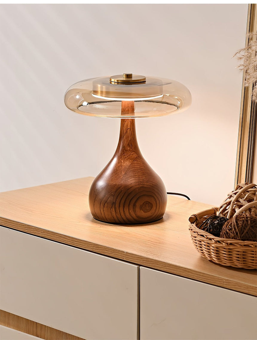 Table lamp with a glass shade lit close on a pale wood surface