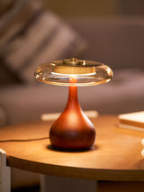 Table lamp with a glass shade lit on a round wood table at dusk