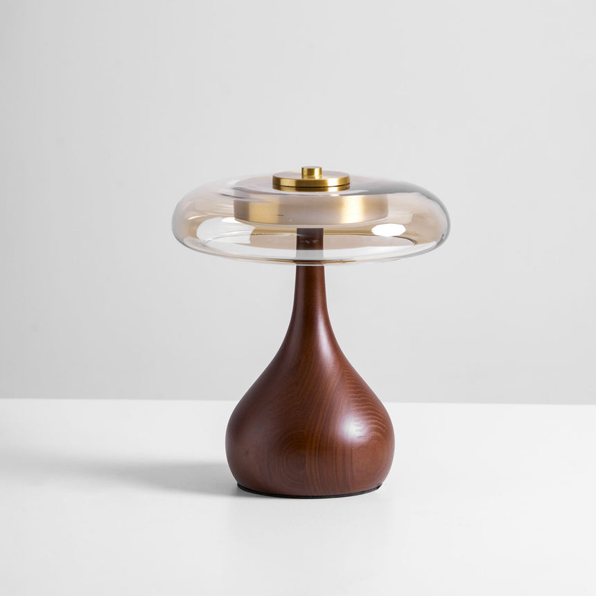 The short glass shade table lamp lit against a plain pale ground