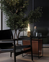 Table lamp with night light lit on a dark table beside an olive tree