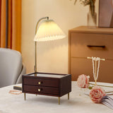 Table lamp with storage lit on a dresser beside jewelry and flowers