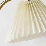 Close view of the pleated shade hanging from the curved brass arch