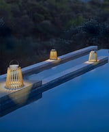 The lantern lit on the coping of a pool with the water lit blue beyond