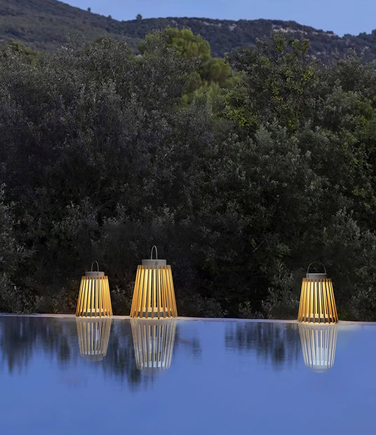 Three lanterns lit on a pool edge with a dark hillside behind them