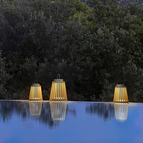 Three lanterns lit on a pool edge with their reflection and planting