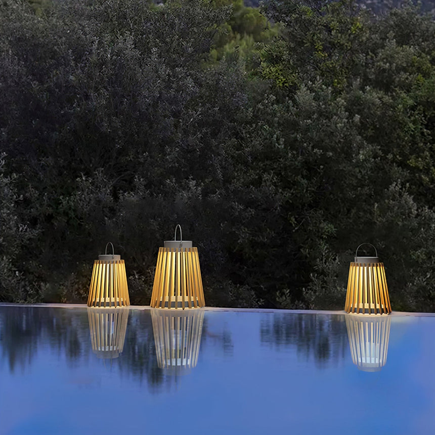 Three lanterns lit on a pool edge with their reflection and planting