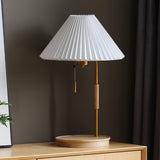 The same lamp with a beige pleated shade, lit on a wood cabinet