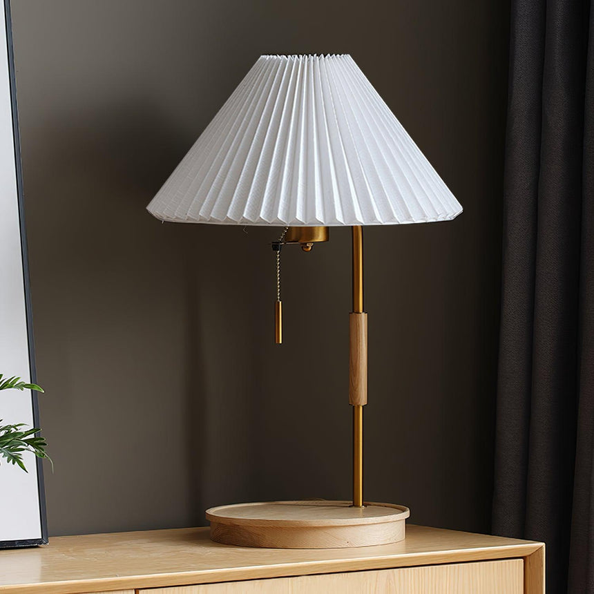 The same lamp with a beige pleated shade, lit on a wood cabinet