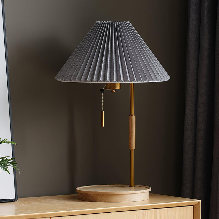 The lamp with a gray pleated shade, lit on a wood cabinet