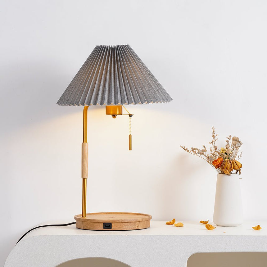 Pleated shade lamp lit warm on a console with petals on the surface