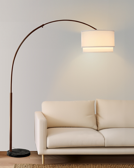 Bronze arc lit beside a cream sofa on a wood floor, shade over the seat