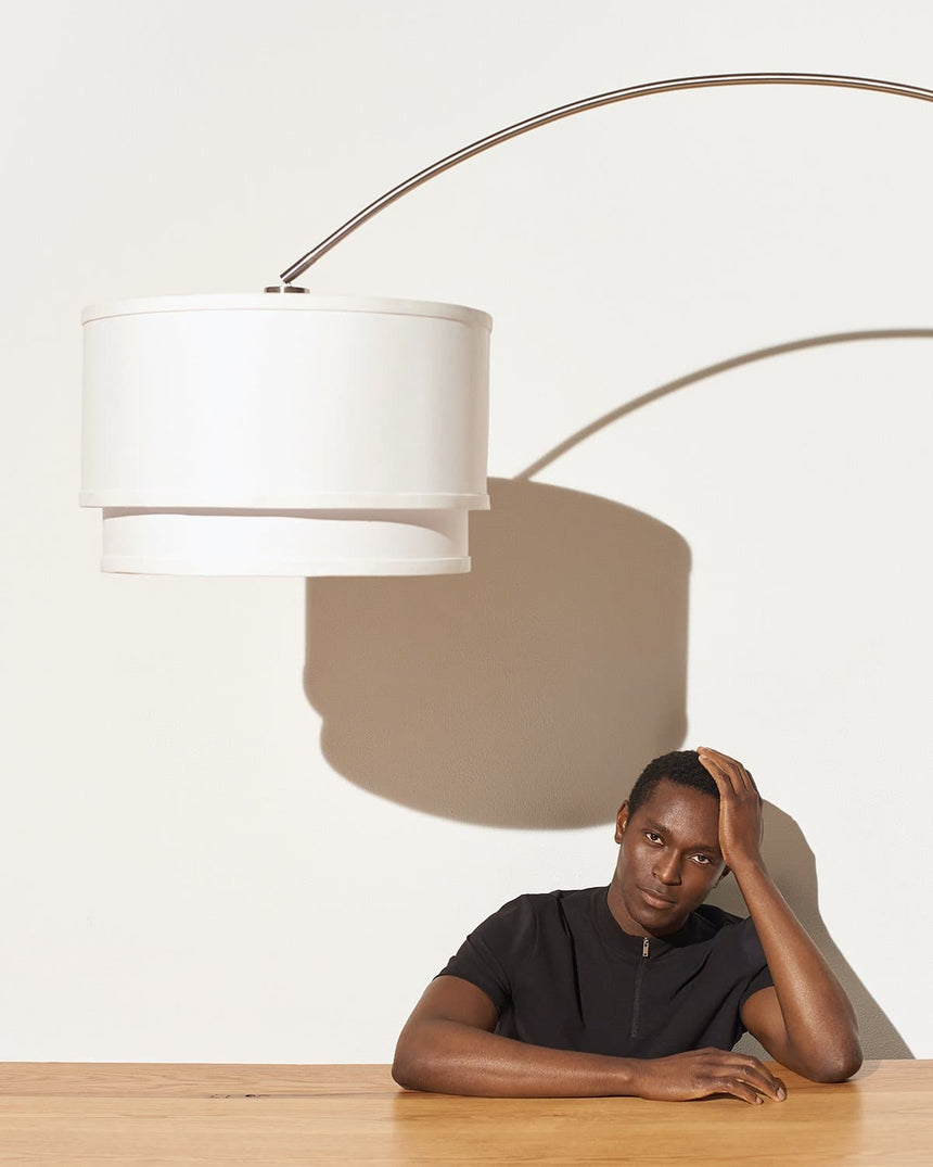 The white shade lit over a wood table with someone seated and reading