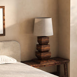 Tall table lamp on a bench beside a bed with a pale headboard