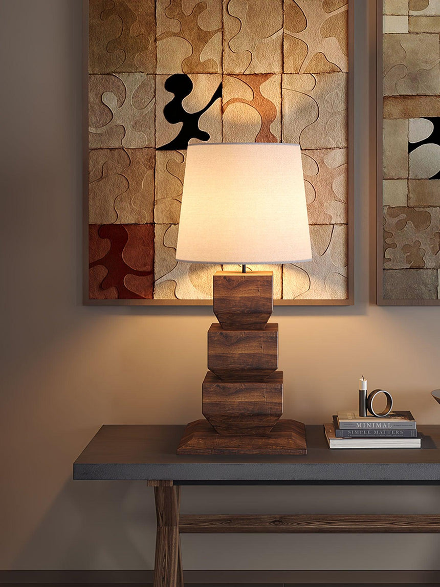 Tall table lamp lit on a dark console below a framed abstract work