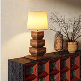 Tall table lamp lit on a dark console beside branches in a stone vase