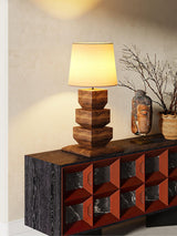Tall table lamp lit on a console in the corner of a pale room