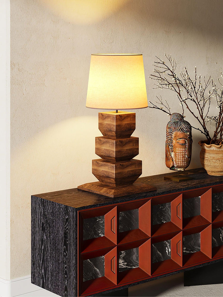 Tall table lamp lit on a console in the corner of a pale room