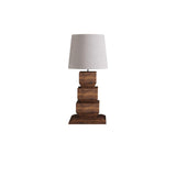 Tall table lamp seen at a distance, white drum shade over the wood stack